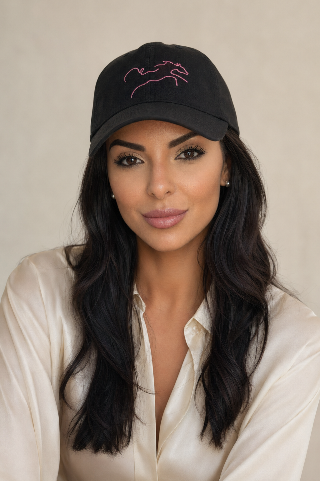 A person wearing a black baseball cap with pink embroidery and a cream shirt.
