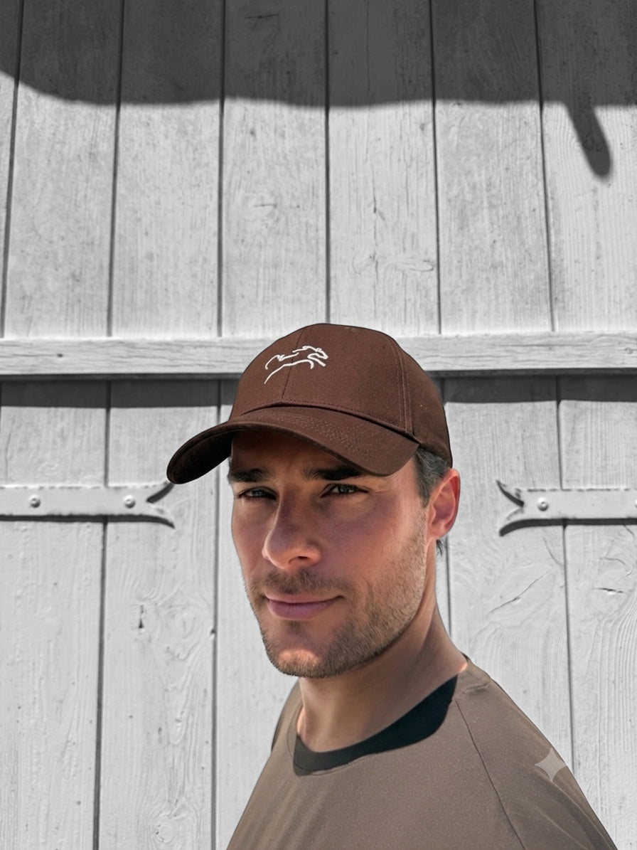 A person wearing the Coco Cap, a brown baseball cap, outdoors.