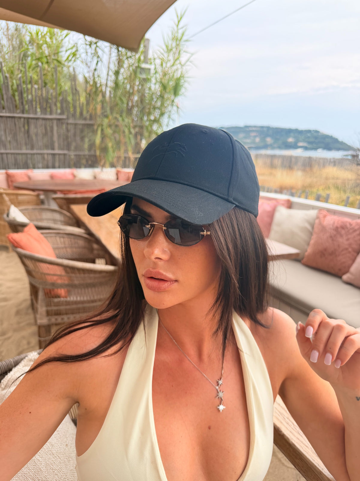 A person wearing the Core Cap, a black baseball cap, outdoors by the sea.
